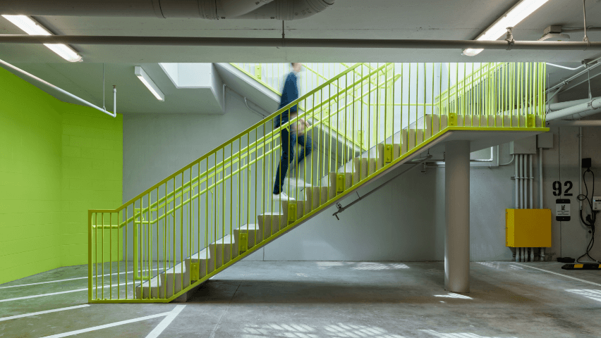A blurred figure walking up lime green stairs in an underground car park