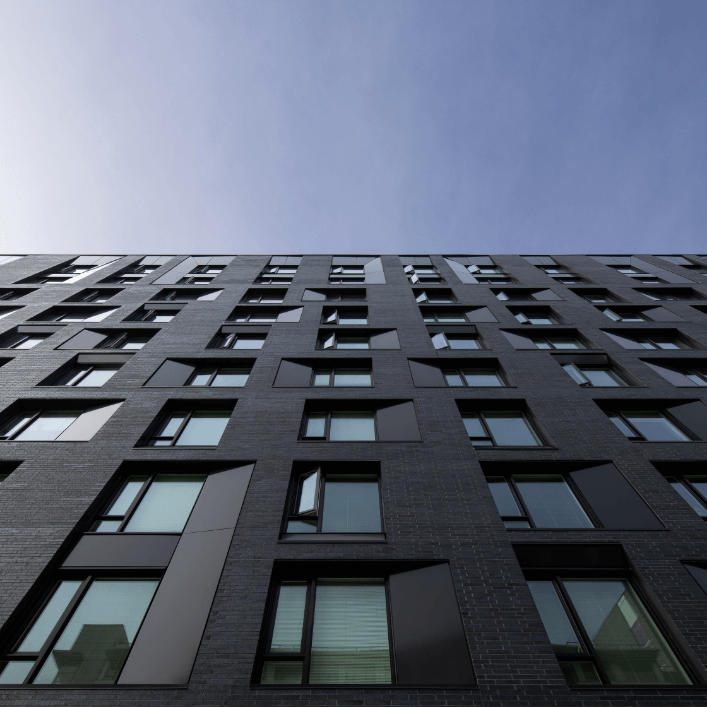 A photo taken very close to a modern building looking up at gleaming windows against a blue sky